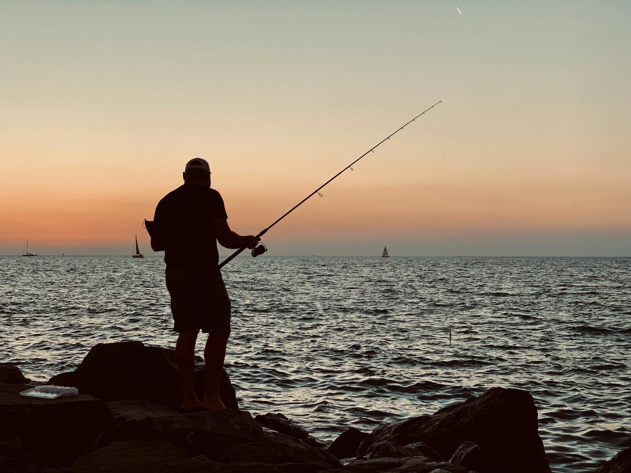 A man fishing on the rocks at sunset
